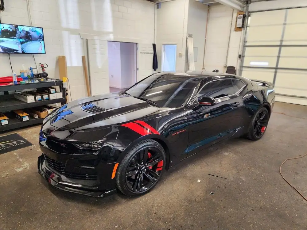Black Chevrolet Camaro with tinted windows in the install bay beside film rolls