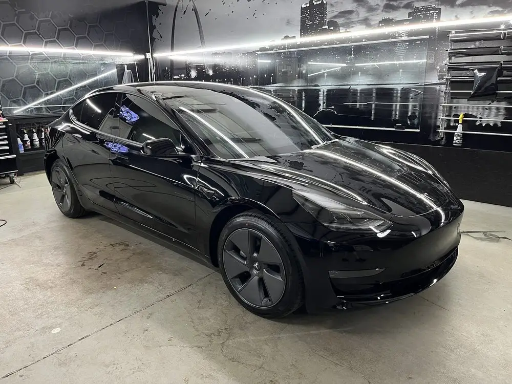 Black Tesla Model 3 with window tint in the showroom beside a St. Louis skyline mural