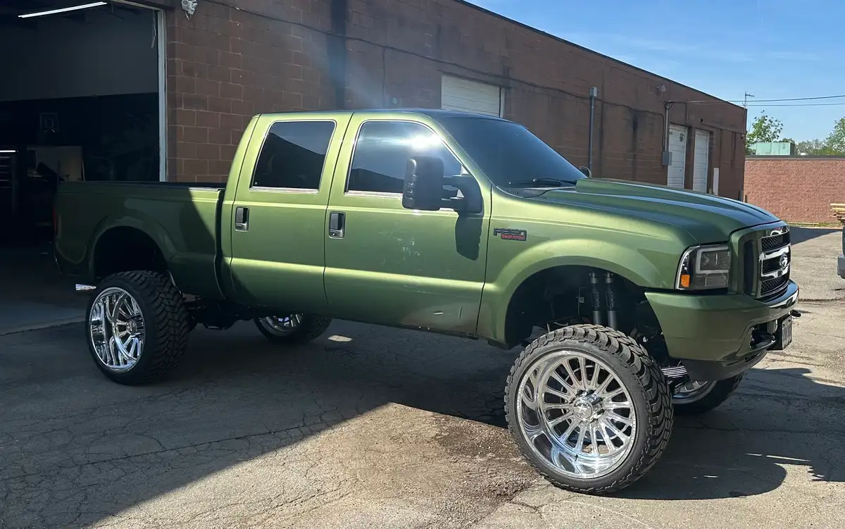 Lifted green Ford F-250 pickup with tinted cab windows outside the shop