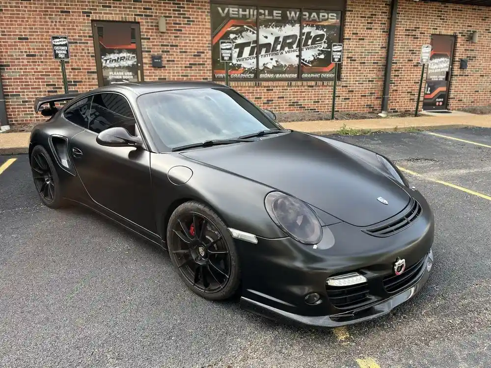 Matte black Porsche 911 Turbo with tinted windows in front of the shop